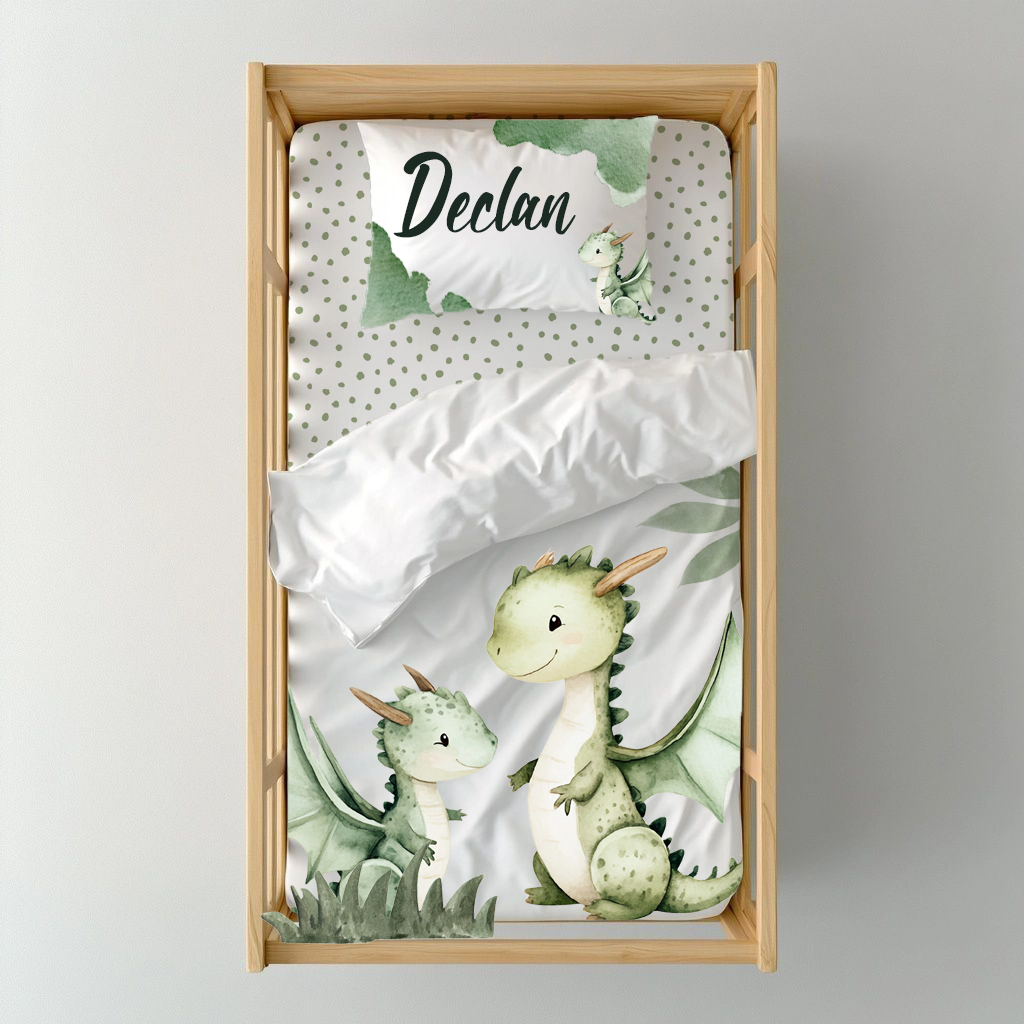 Dragon Dreams cot duvet cover featuring two sweet green dragons with soft leafy details, sage green accents and a coordinating dotted pillow on a clean white background | Dragon Dreams bababed-duvetoortreksel met twee oulike groen drakies, sagte blaardetail, saliegroen aksente en ’n bypassende kolletjie-kussing op ’n skoon wit agtergrond.