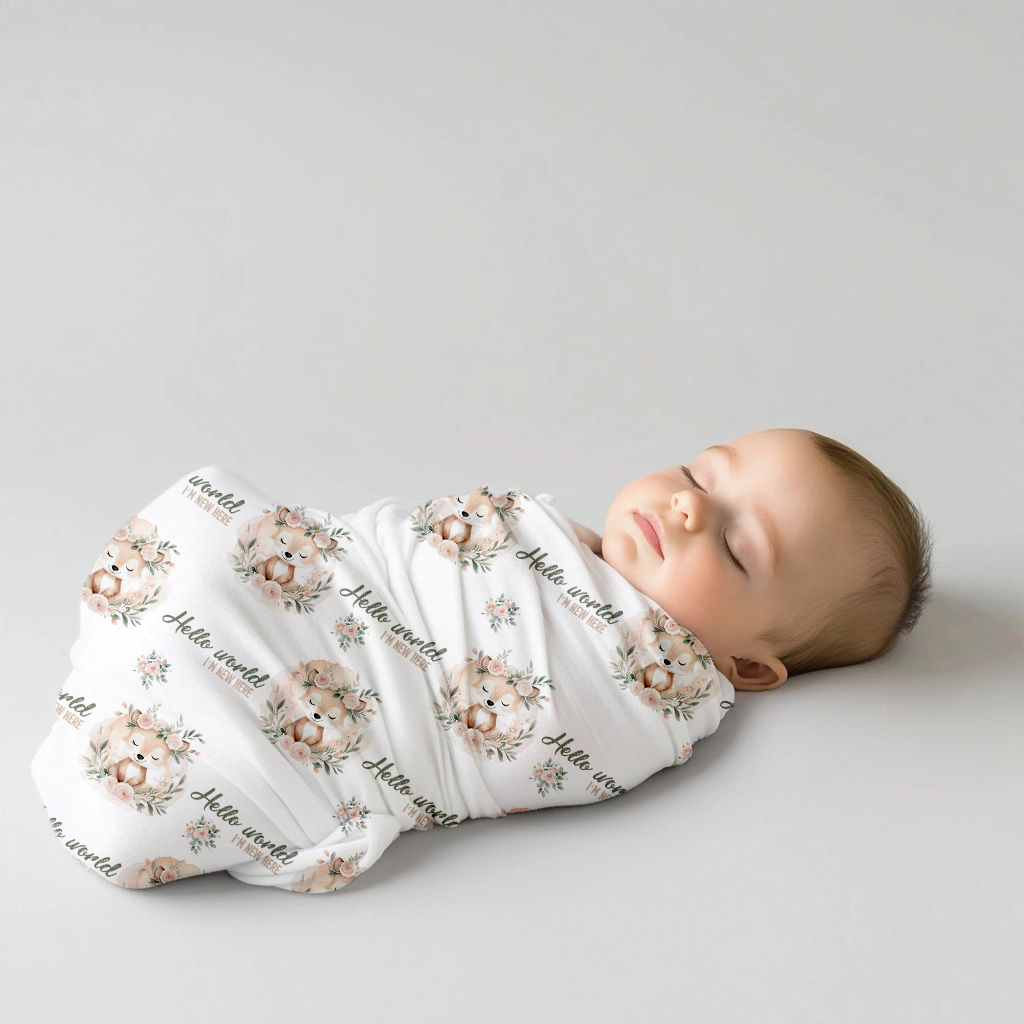 Fawn & Flora baby swaddle set featuring sweet sleeping fawns, blush pink florals, soft greenery and “Hello world I’m new here” details on a white background | Fawn & Flora baba-inbakerstel met oulike slapende takbokke, sagte pienk blomme, groen blare en “Hello world I’m new here”-detail op ’n wit agtergrond.