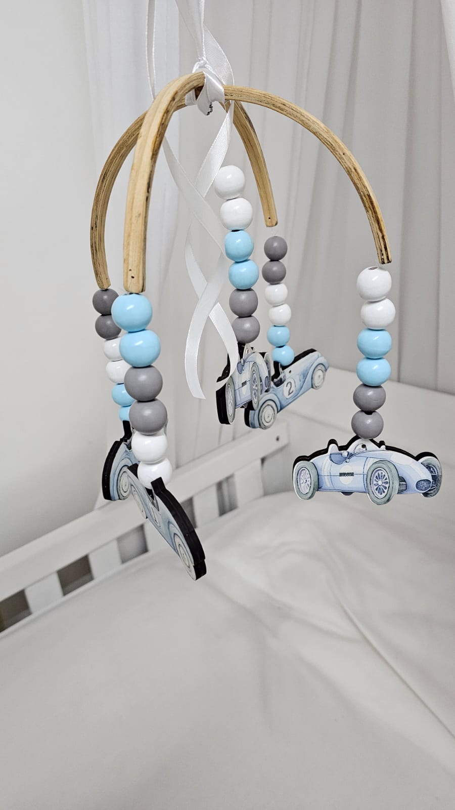 Baby crib mobile with wooden arch, beads, and toy cars in a nursery setting.