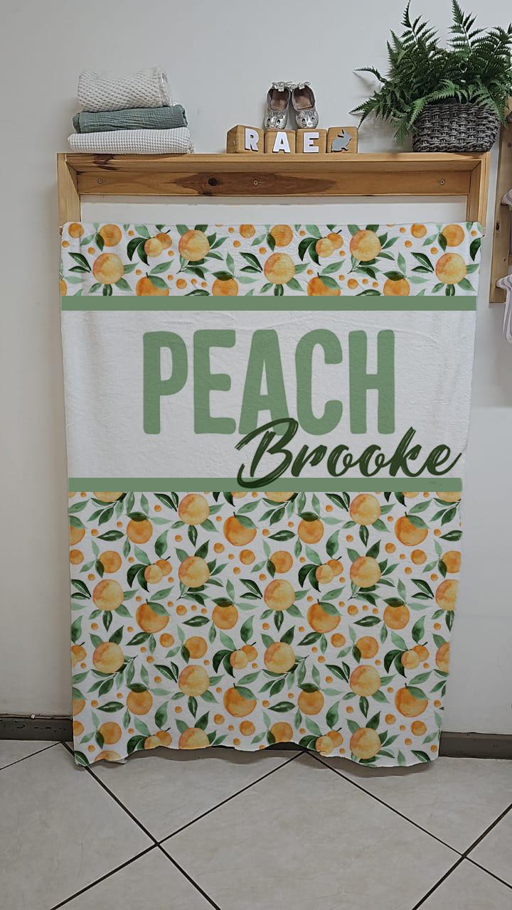 Peachy fleece blanket featuring a fresh peach fruit pattern with green leaves on a white background in soft warm nursery tones | Peachy fleece-kombers met ’n vars perskevrug-patroon en groen blare op ’n wit agtergrond in sagte warm kinderkamer-kleure.