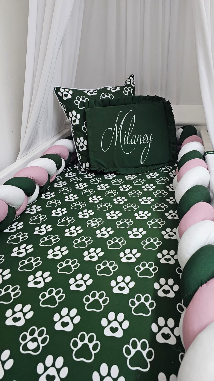 Bedding set with paw print pattern and a pillow with 'Milaney' on it, against a white curtain background.