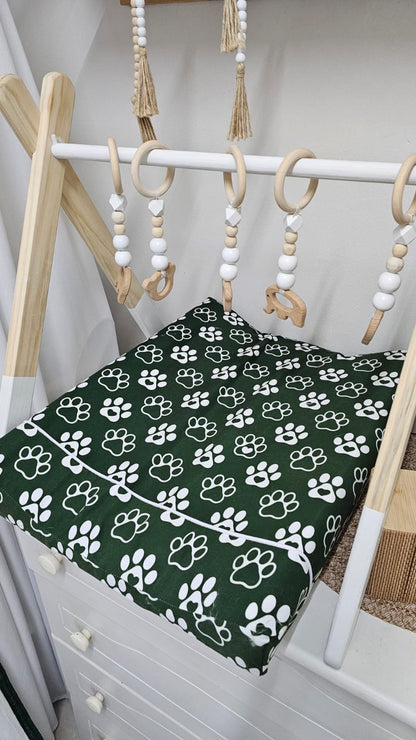 Crib with green and white paw print sheet and hanging baby toys.