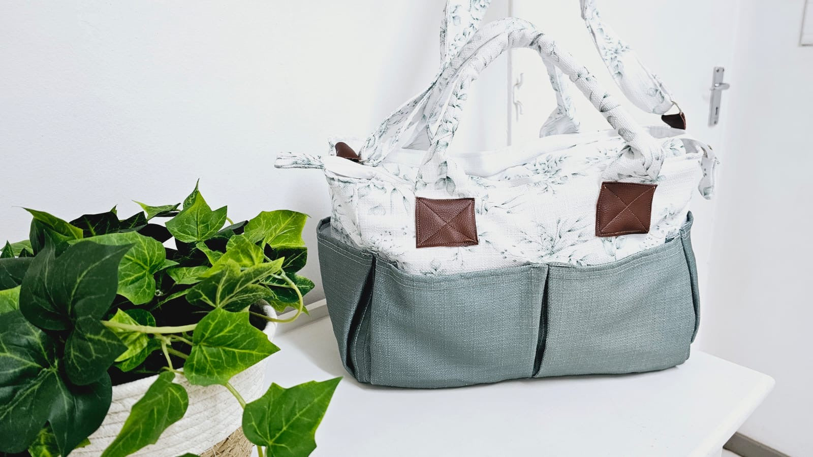 Gray and white patterned baby carrier on a white surface with green leaves in the background