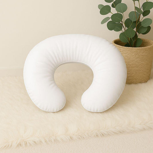 White U-shaped nursing pillow on a beige surface with a plant in the background