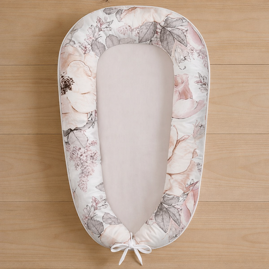 Blissful Blossom baby nest featuring soft blush pink flowers and grey leaves, photographed flat lay on wooden surface
