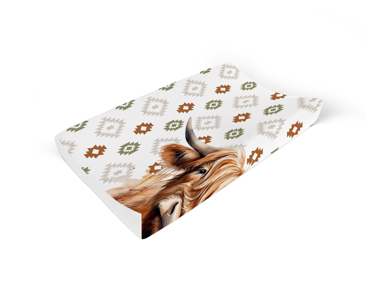 Boho Highlands Cow changing mat cover featuring a large Highland cow with geometric boho patterns in rust, olive green and soft neutral tones on a white background | Boho Highlands-bees aantrekmat-oortreksel met ’n groot Highland-bees en geometriese boho-patrone in roes, olyfgroen en sagte neutrale kleure op ’n wit agtergrond.