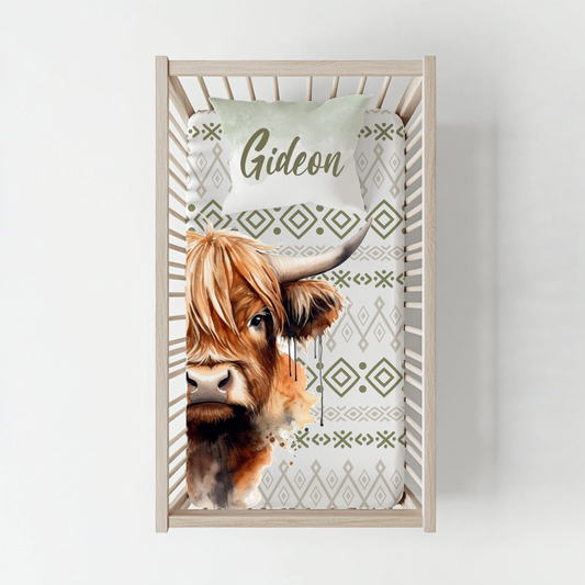 Boho Highlands Cow cot duvet cover featuring a large Highland cow illustration with olive green and neutral geometric boho patterns on a clean white background | Boho Highlands-bees bababed-duvetoortreksel met ’n groot Highland-bees illustrasie en olyfgroen en neutrale geometriese boho-patrone op ’n skoon wit agtergrond.