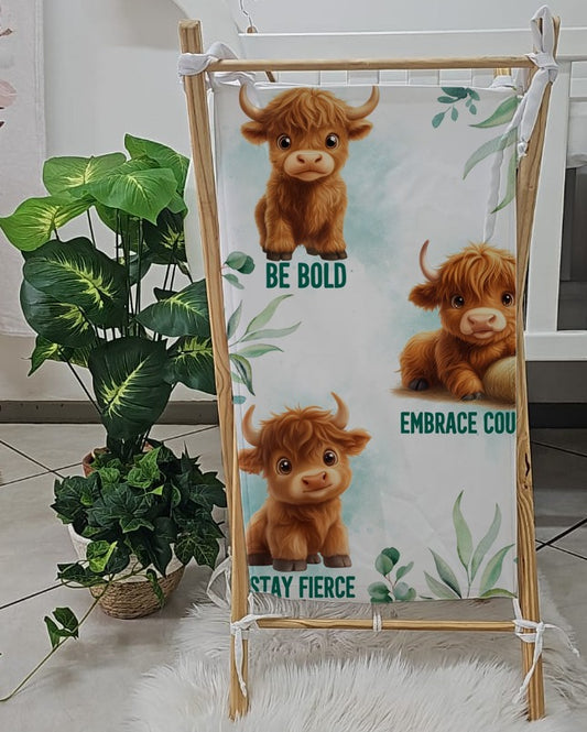 Brave and Bold laundry basket featuring sweet Highland cows, soft green botanical details and motivational phrases including “Stay Fierce” and “Embrace Courage” | Brave and Bold wasgoedmandjie met oulike Highland-beeste, sagte groen botaniese detail en motiverende frases insluitend “Stay Fierce” en “Embrace Courage”.