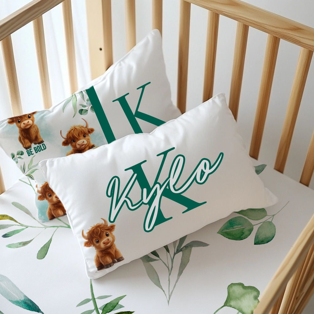 Brave and Bold personalised nursery pillow set featuring sweet Highland cows, green botanical leaves, a large initial “K” and a name cushion personalised with “Kyle” | Brave and Bold gepersonaliseerde kinderkamer-kussingstel met oulike Highland-beeste, groen botaniese blare, ’n groot voorletter “K” en ’n naamkussing gepersonaliseer met “Kyle”.