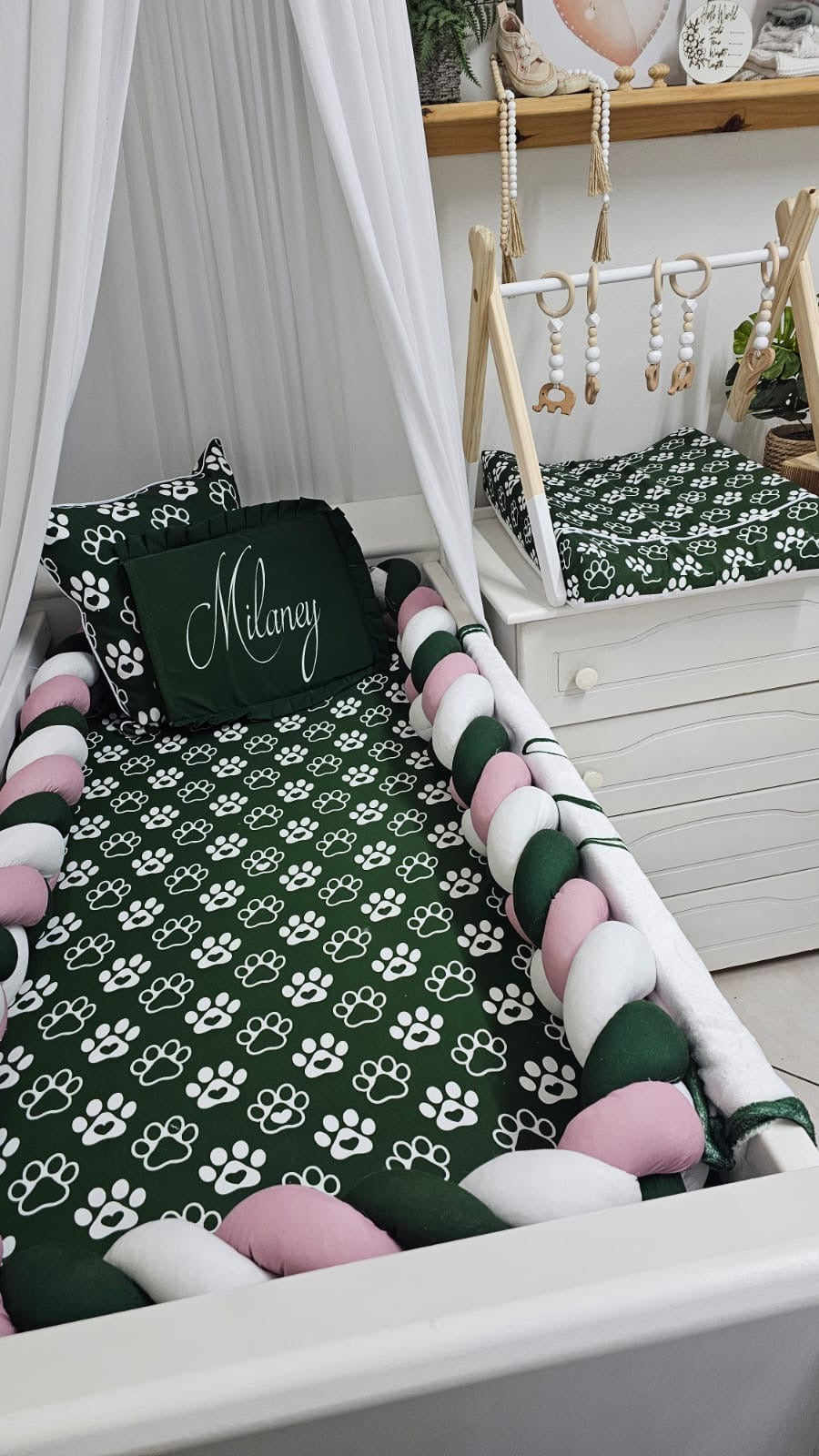 Children's crib with green and white paw print bedding, pink pom-poms, and a white canopy.