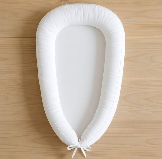 Plain white custom baby nest designed for personalised nursery themes, photographed flat lay on wooden surface
