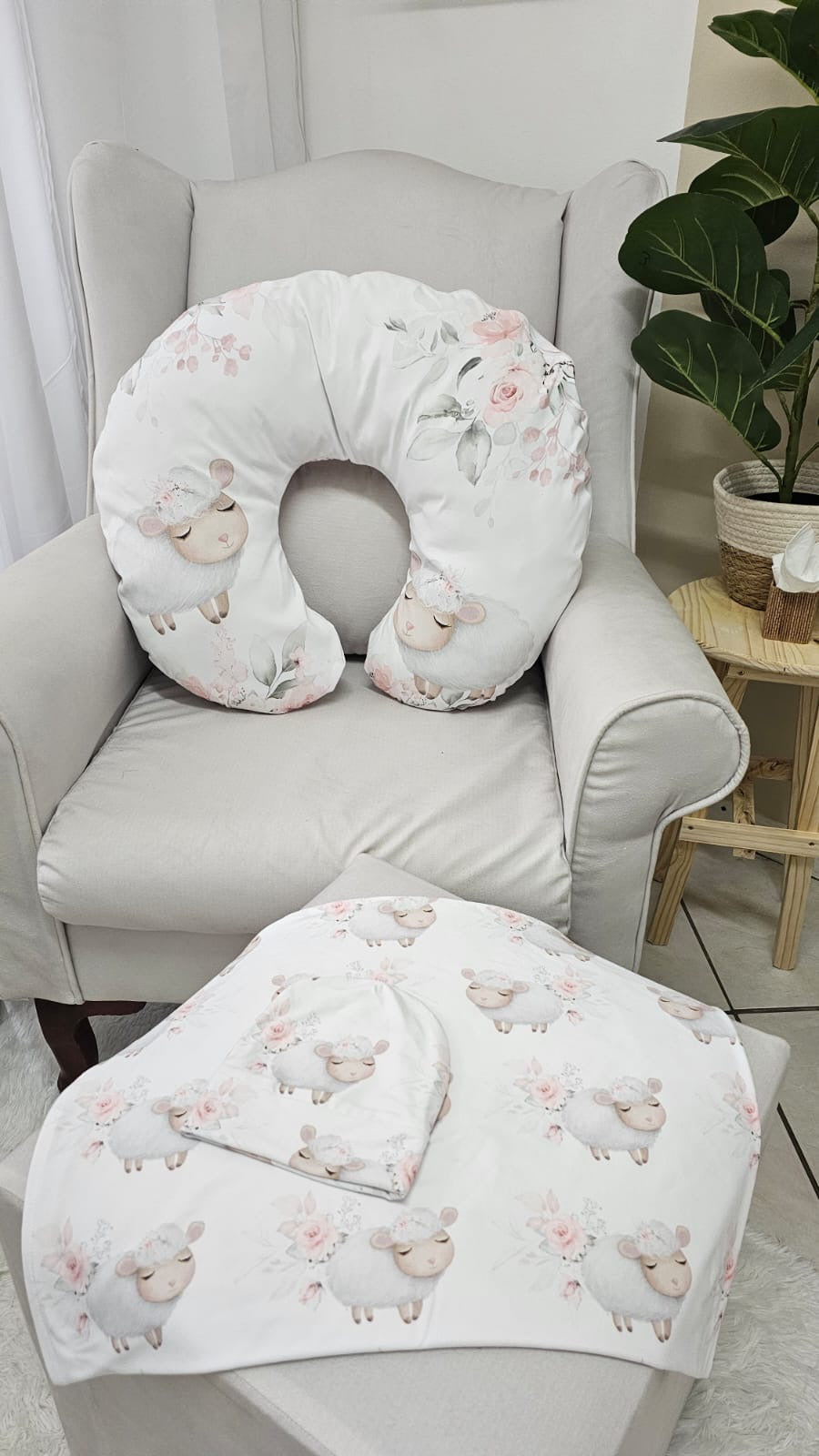 Floral-patterned U-shaped pillow and matching blanket on a chair with a plant in the background.