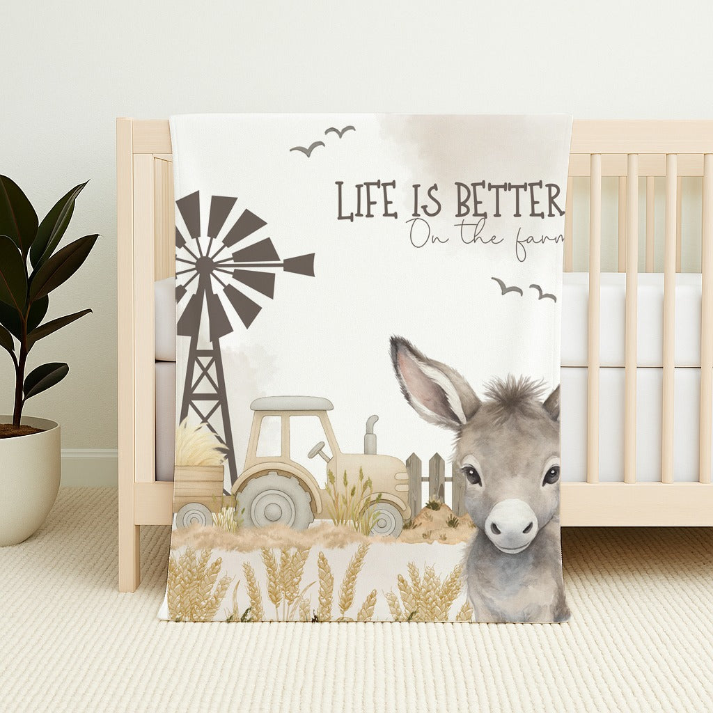 Donkey Dreams fleece blanket featuring a sweet donkey, tractor, windmill and soft neutral farm scene with the words “Life is better on the farm” | Donkey Dreams fleece-kombers met ’n oulike donkie, trekker, windpomp en sagte neutrale plaastoneel met die woorde “Life is better on the farm”.