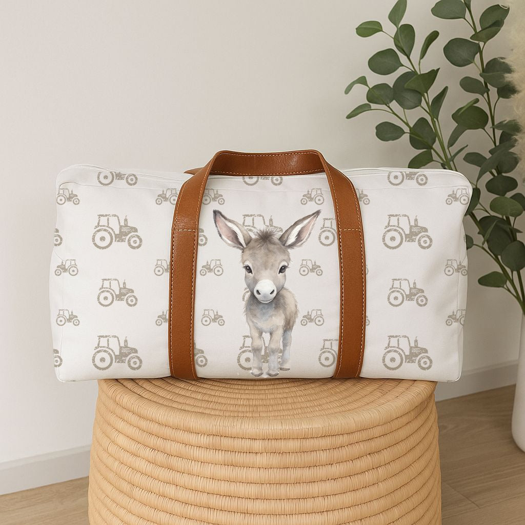 Donkey Dreams hospital bag featuring a sweet grey donkey with a soft neutral tractor pattern and tan handles, perfect for baby essentials | Donkey Dreams hospitaaltas met ’n oulike grys donkie, sagte neutrale trekkerpatroon en bruin handvatsels, perfek vir baba-benodigdhede.