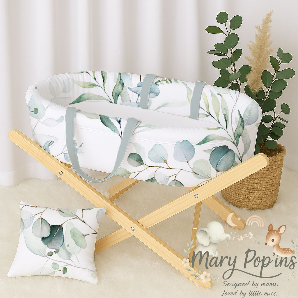 Eucalyptus carry cot featuring a soft green and sage leafy print with grey handles, styled on a natural wooden stand with a matching cushion | Eucalyptus draagwieg met ’n sagte groen en saliegroen blaarpatroon en grys handvatsels, gestileer op ’n natuurlike houtstaander met ’n bypassende kussing.