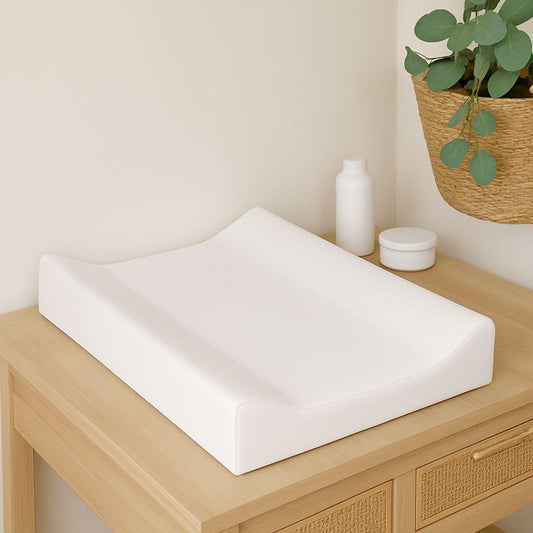 White bay changing mattress on a wooden surface with a plant in the background