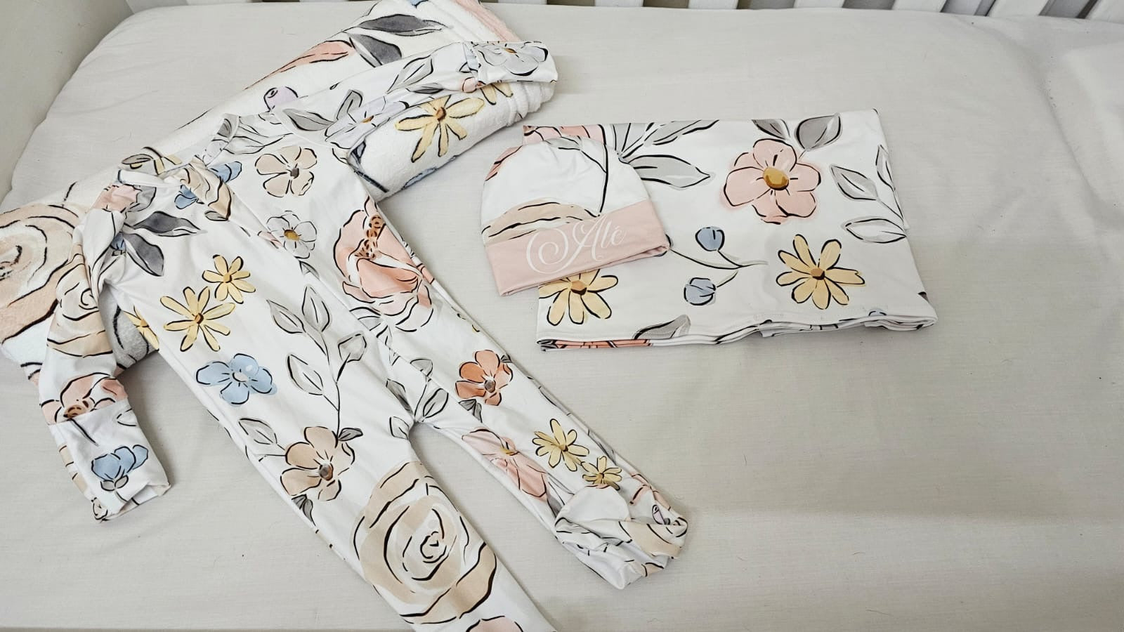 Floral-patterned baby items including a hat, bib, and blanket on a light background