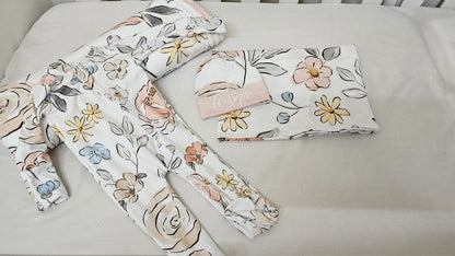 Floral-patterned baby items including a hat, bib, and blanket on a light background