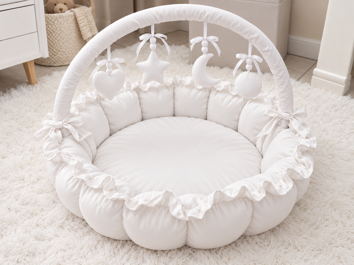 A white padded baby play mat with a ruffled border, a curved support arch, and hanging baby toys including a heart, star, and crescent moon, shown on a white rug in a nursery setting.