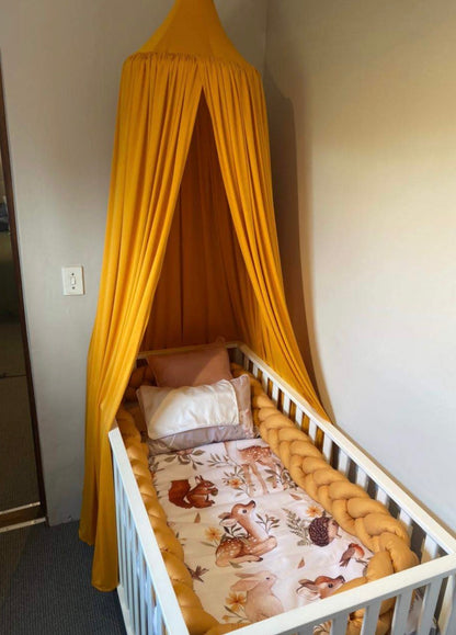 Children's crib with yellow canopy and animal-patterned bedding in a room.