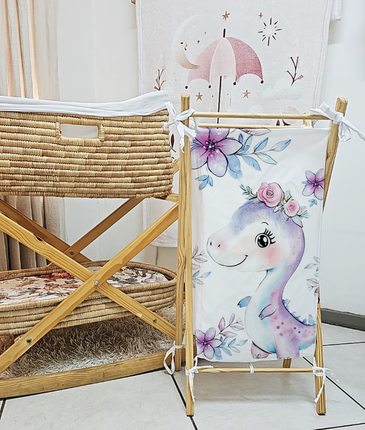 Girl Dino laundry basket featuring a sweet pastel purple and blue dinosaur with a pink floral crown, surrounded by soft pink and blue flowers | Girl Dino wasgoedmandjie met ’n oulike pastelpers en blou dinosourus met ’n pienk blomkroon, omring deur sagte pienk en blou blomme.