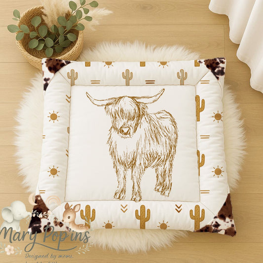 Highlands Trail baby playmat featuring a hand-drawn Highland cow with warm mustard cactus, sun and geometric details, finished with cowhide-style corner accents | Highlands Trail baba-speelmat met ’n handgetekende Highland-bees, warm mosterdkleurige kaktusse, son- en geometriese detail, afgewerk met beesvel-styl hoekaksente.