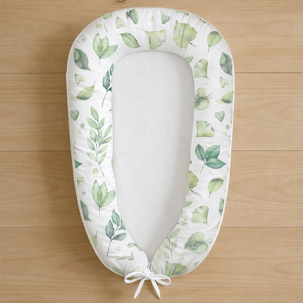 Leafy Love baby nest featuring watercolour green leaves on white fabric, photographed flat lay on wooden surface
