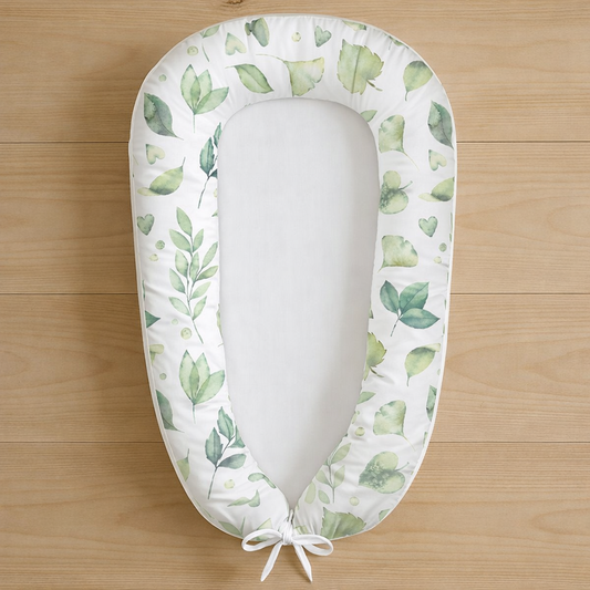 Leafy Love baby nest featuring watercolour green leaves on white fabric, photographed flat lay on wooden surface
