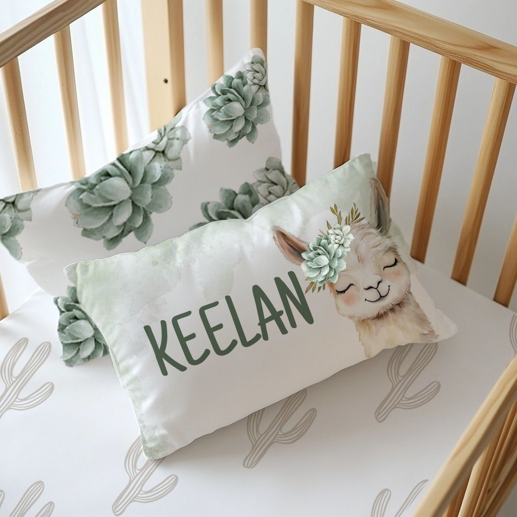 Neutral Succulents Llama personalised nursery pillow featuring a sweet smiling llama with a soft sage succulent crown and the name “Keelan” in dark green lettering | Neutrale Vetplante Lama gepersonaliseerde kinderkamer-kussing met ’n oulike glimlaggende lama, ’n sagte saliegroen vetplantkroon en die naam “Keelan” in donkergroen letters.