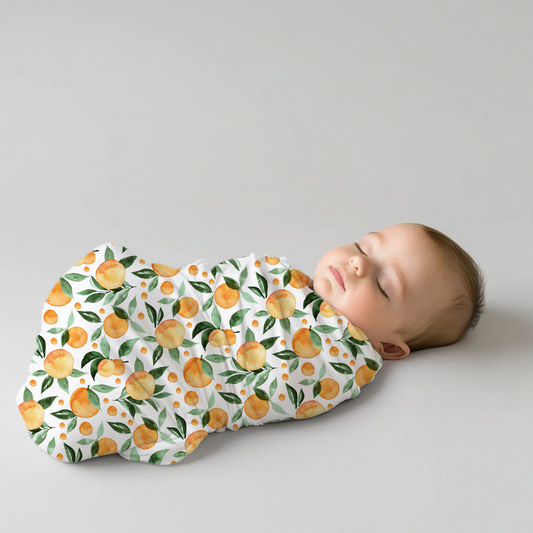 Peachy Goose baby swaddle set featuring a fresh peach and green leaf print on a white background, wrapped snugly around a newborn baby | Peachy Goose baba-inbakerstel met ’n vars perske- en groen blaarpatroon op ’n wit agtergrond, knus om ’n pasgebore baba toegedraai.