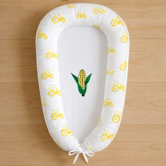 Plaas Lewe baby nest featuring yellow tractors and corn design, photographed flat lay on wooden surface
