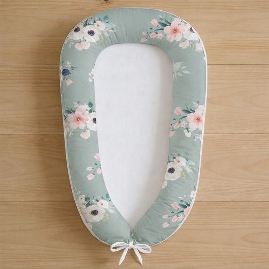 Rainbow Floral baby nest featuring sage green fabric with delicate pink and white flowers, photographed flat lay on wooden surface
