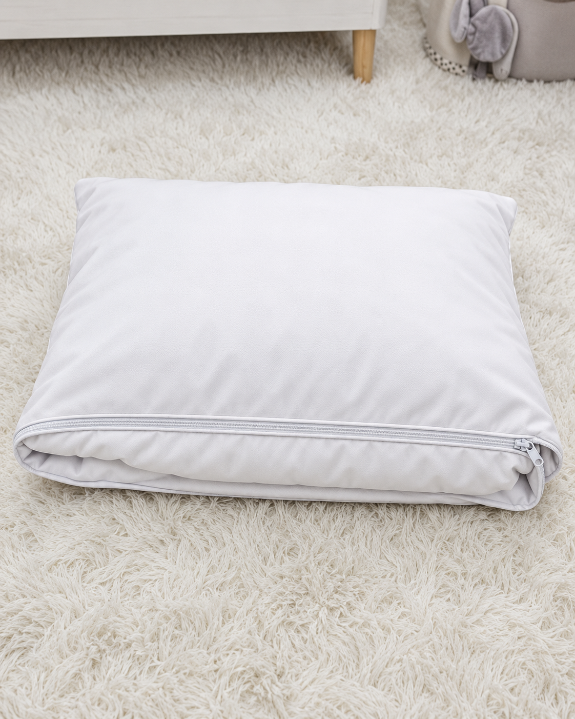 A folded white pillowcase or pillow cover with a zipper closure, resting on a fluffy white shag rug.